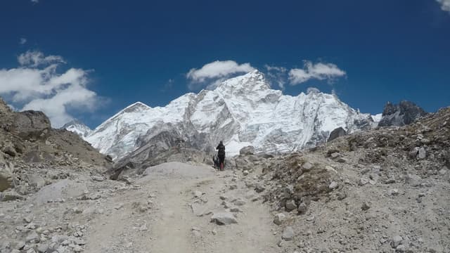 A trekker on a rocky trail below snow peaks