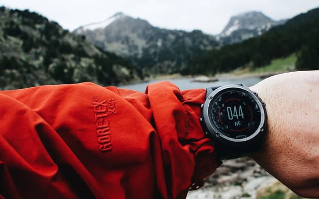 A hiker checking a wrist GPS device on a mountain