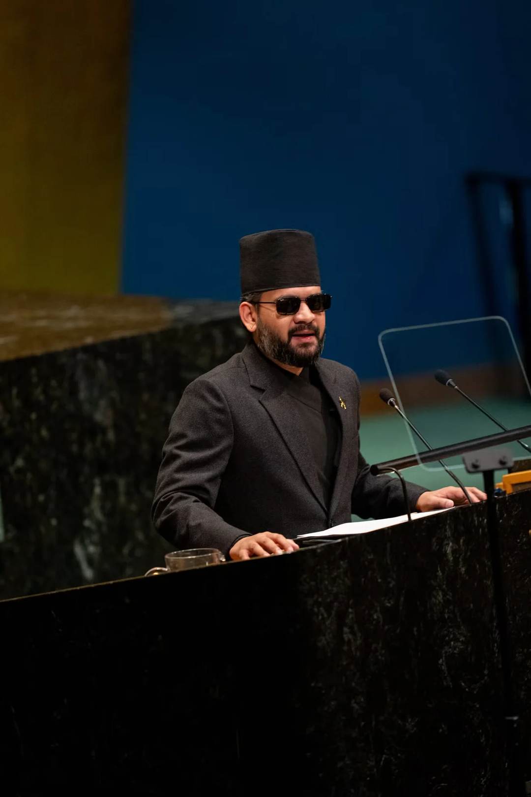 Prime Minister Balen Shah, in a black dhaka topi and sunglasses, speaking at the rostrum of the UN General Assembly hall in New York on 24 September 2026