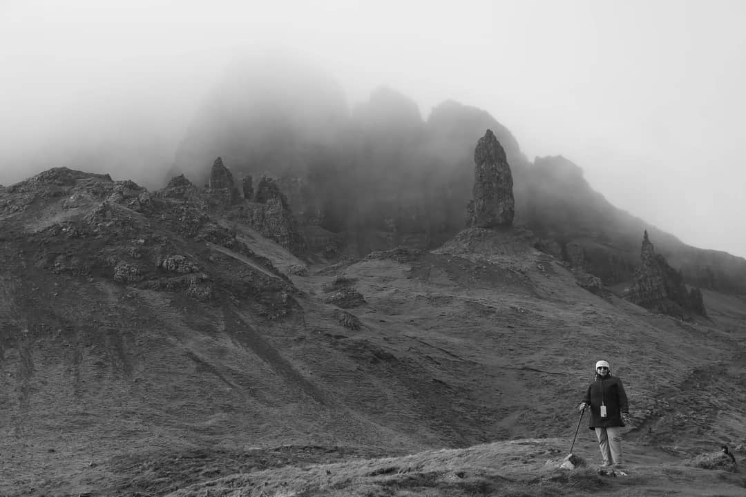 A hiker with trekking poles walking through mist in the Scottish Highlands
