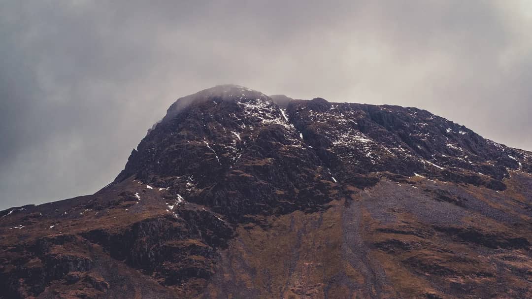 A snow-dusted mountain peak under a moody, cloudy sky