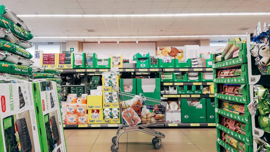A shopping cart in a brightly lit supermarket aisle