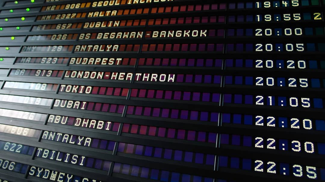 A flip-style airport departure board listing international flights and times