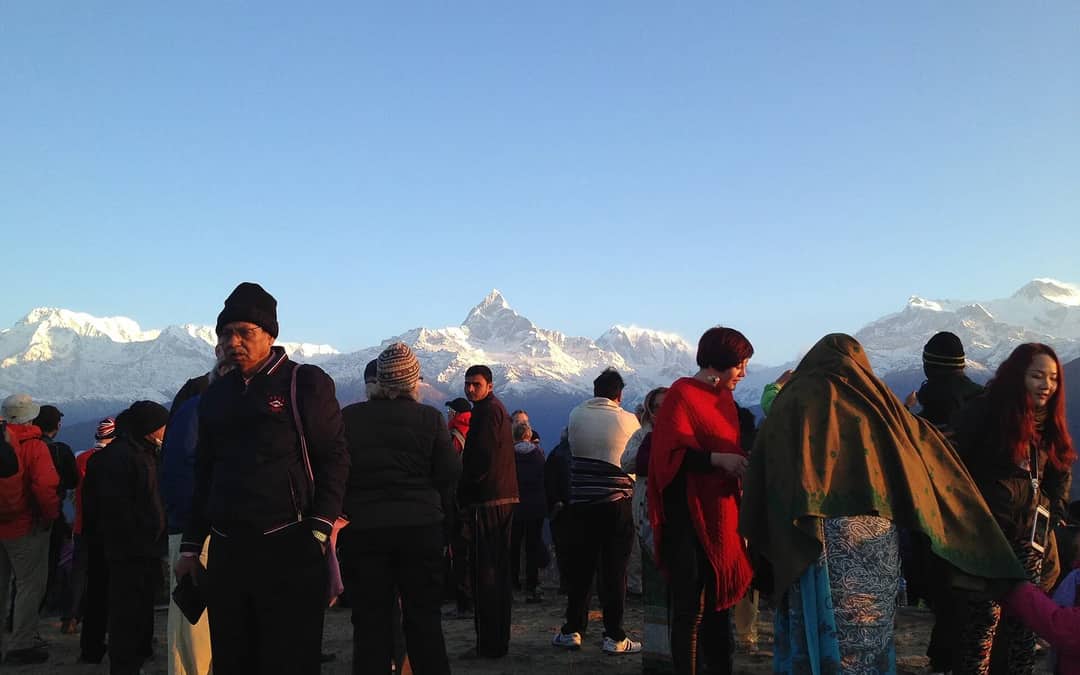 A crowd at a hilltop viewpoint at dawn with Machhapuchhre and the Annapurna range behind them