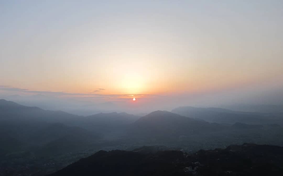 The sun rising over layered hazy hills seen from Sarangkot