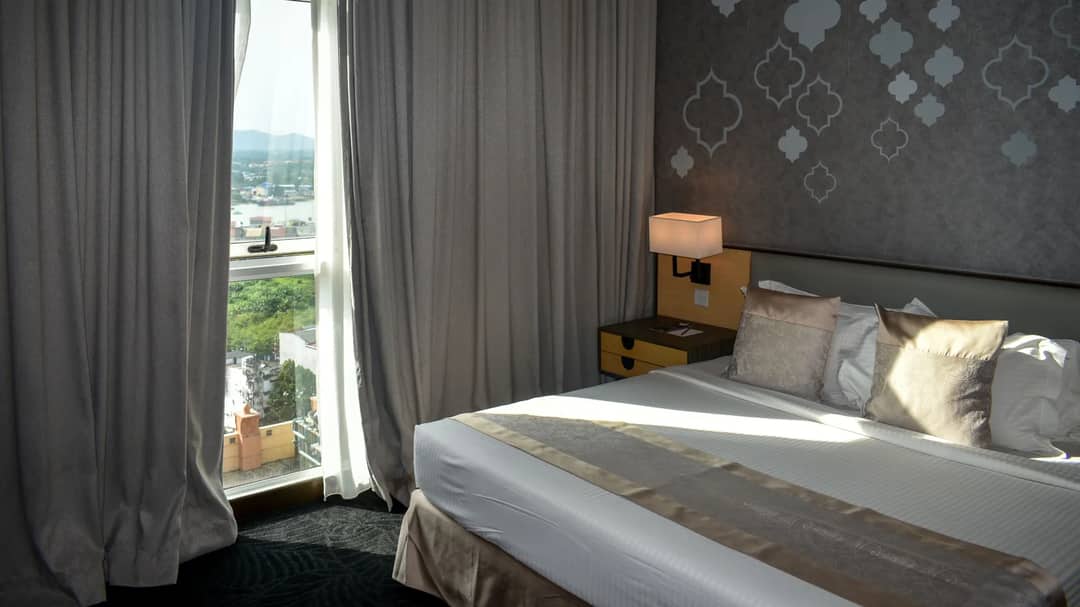 A hotel room with a large window and a view of green hills