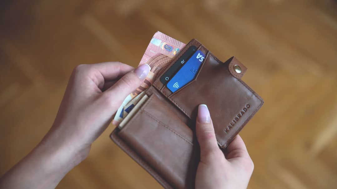 Hands holding a leather wallet with cash and a credit card