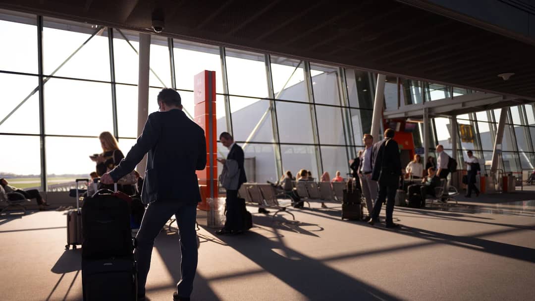 Travellers with carry-on luggage in a sunlit airport terminal waiting for departure