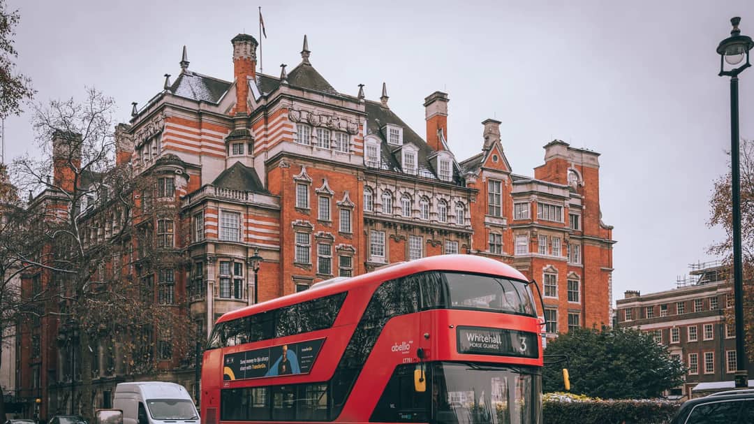 A red double-decker bus on a London street lined with classic buildings