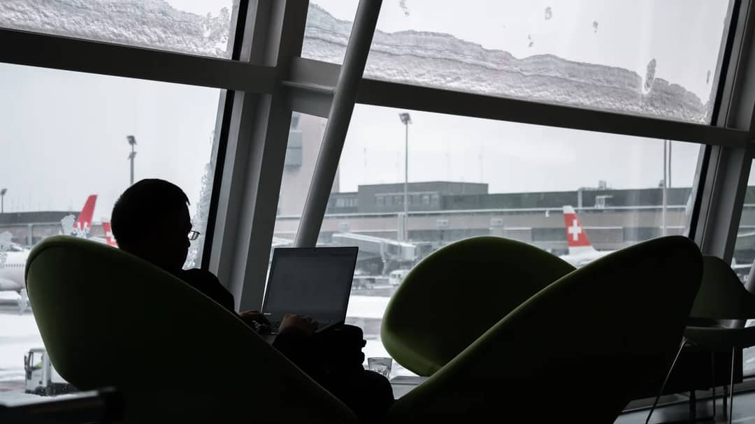 A traveller working on a laptop in an airport lounge with planes outside