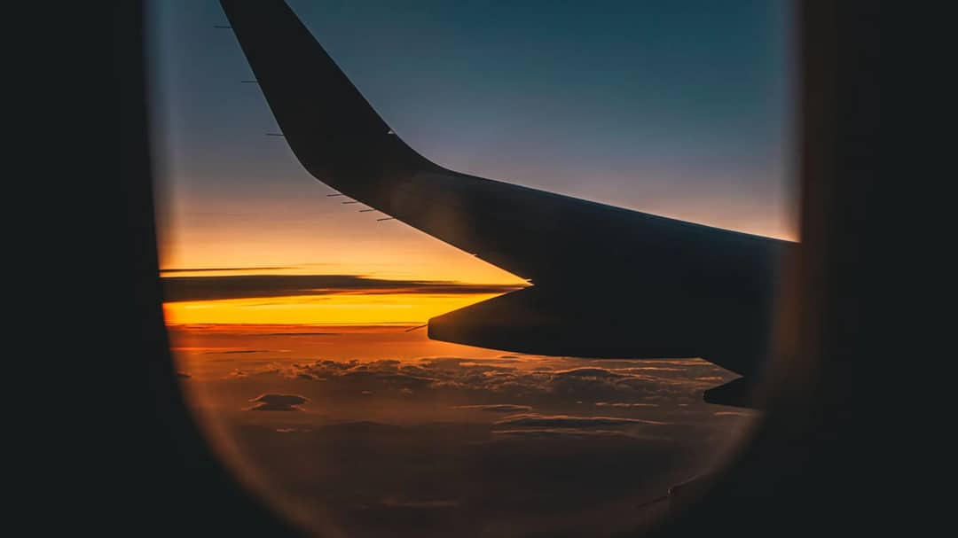 An airplane wing against a sunset sky, seen from a window seat
