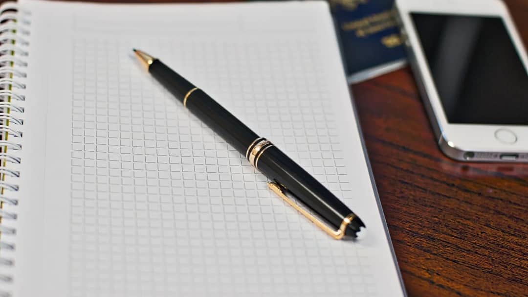 A notebook, pen, smartphone and passport on a wooden desk