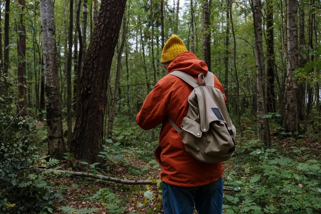 A hiker in an orange jacket with a backpack walking through a green forest