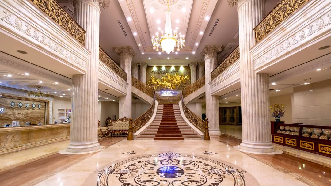 A grand hotel lobby with a marble floor, staircase and chandelier