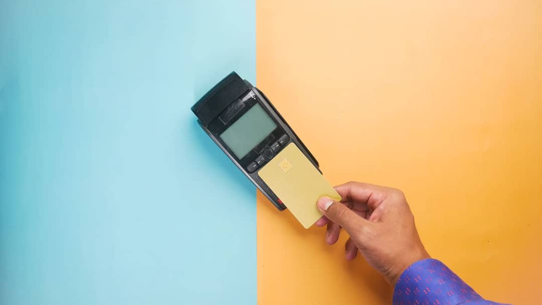 A hand tapping a card on a payment terminal at a shop counter