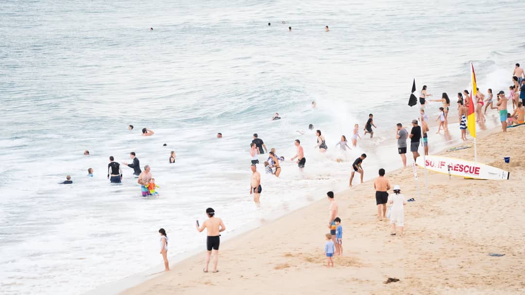 A busy beach at Wollongong in Australia with surf rescue flags on the sand