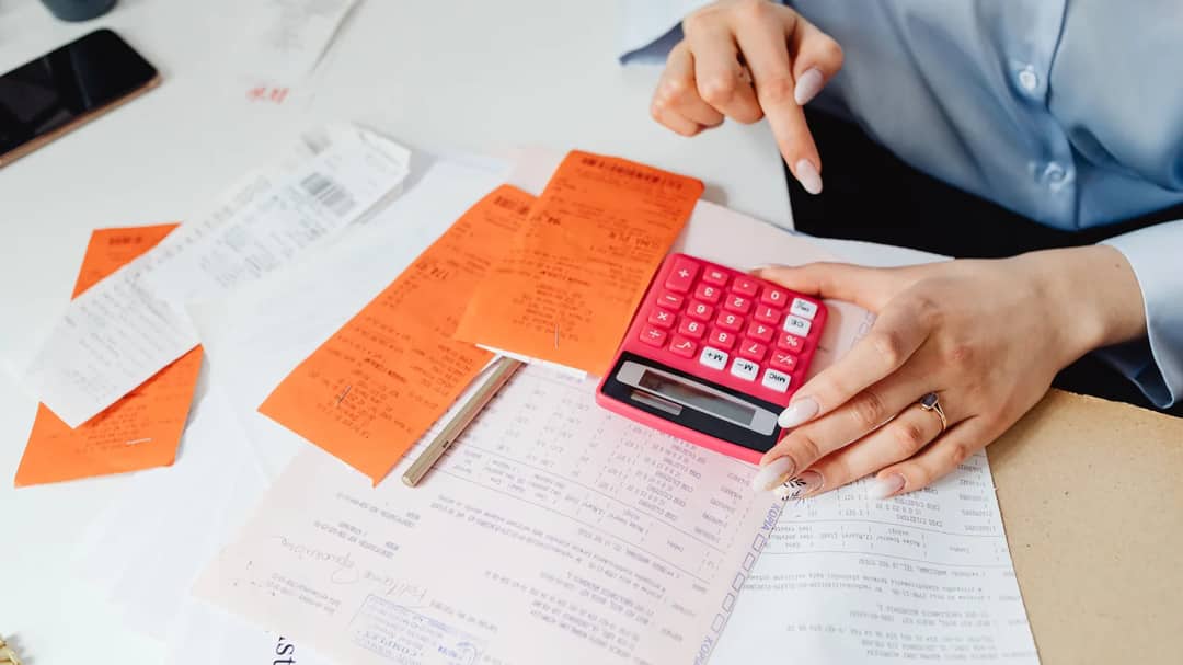 A person working out expenses with a calculator and a pile of receipts at a desk