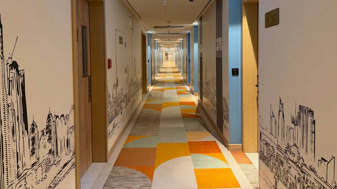 A long, brightly lit hotel corridor with patterned carpet