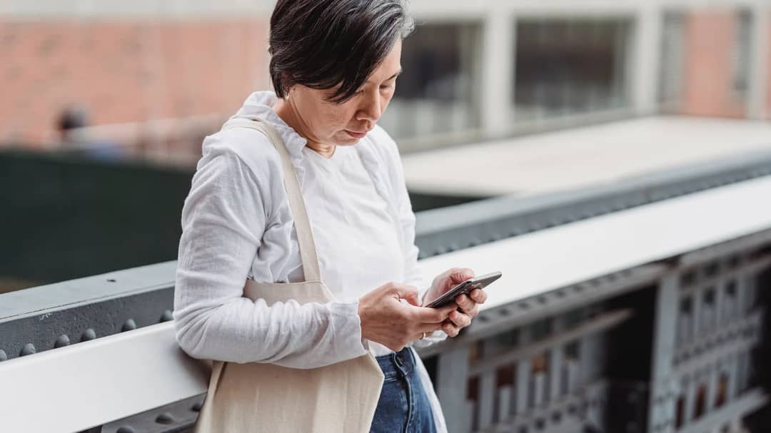 A woman leaning on a railing outdoors and typing on her phone