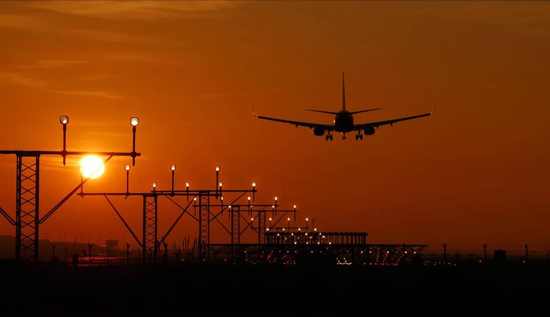 A jet over the runway approach lights at sunset