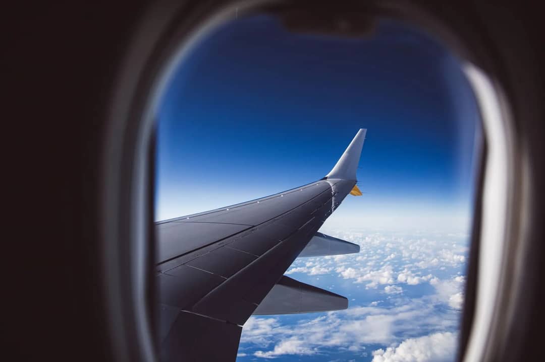 A view from an airplane window of the wing above a layer of clouds in daylight