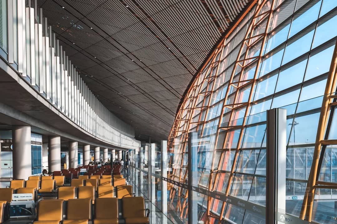 Interior view of a modern airport terminal with seating and large windows letting in natural light.
