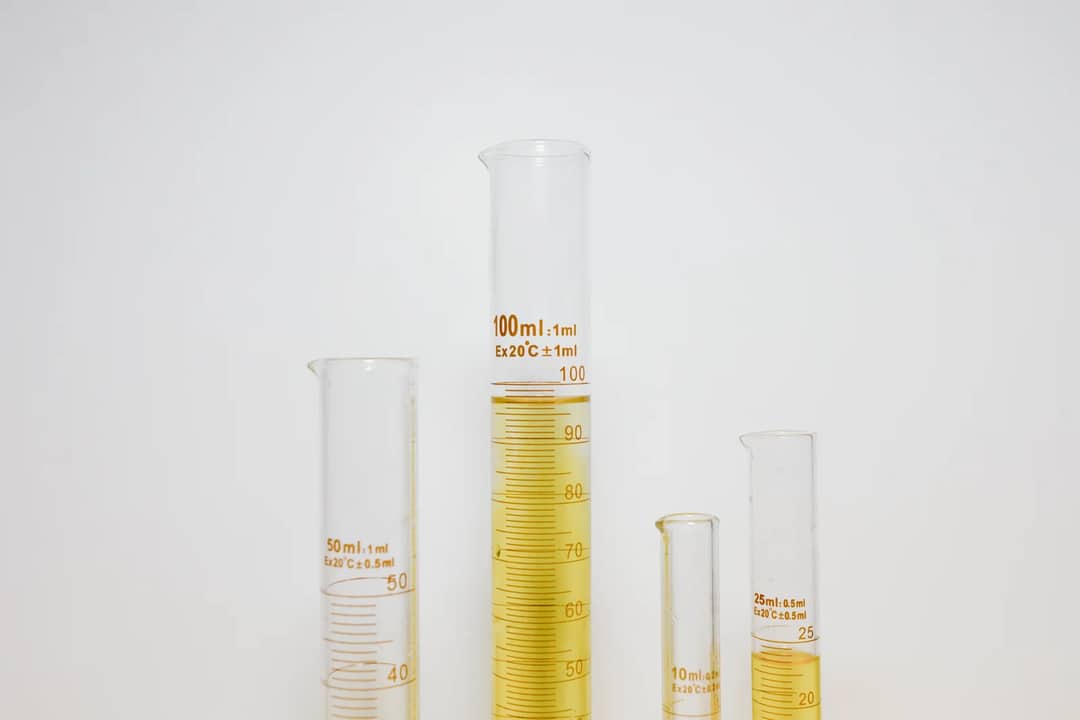 Close-up of graduated cylinders filled with yellow liquid in a laboratory setting.