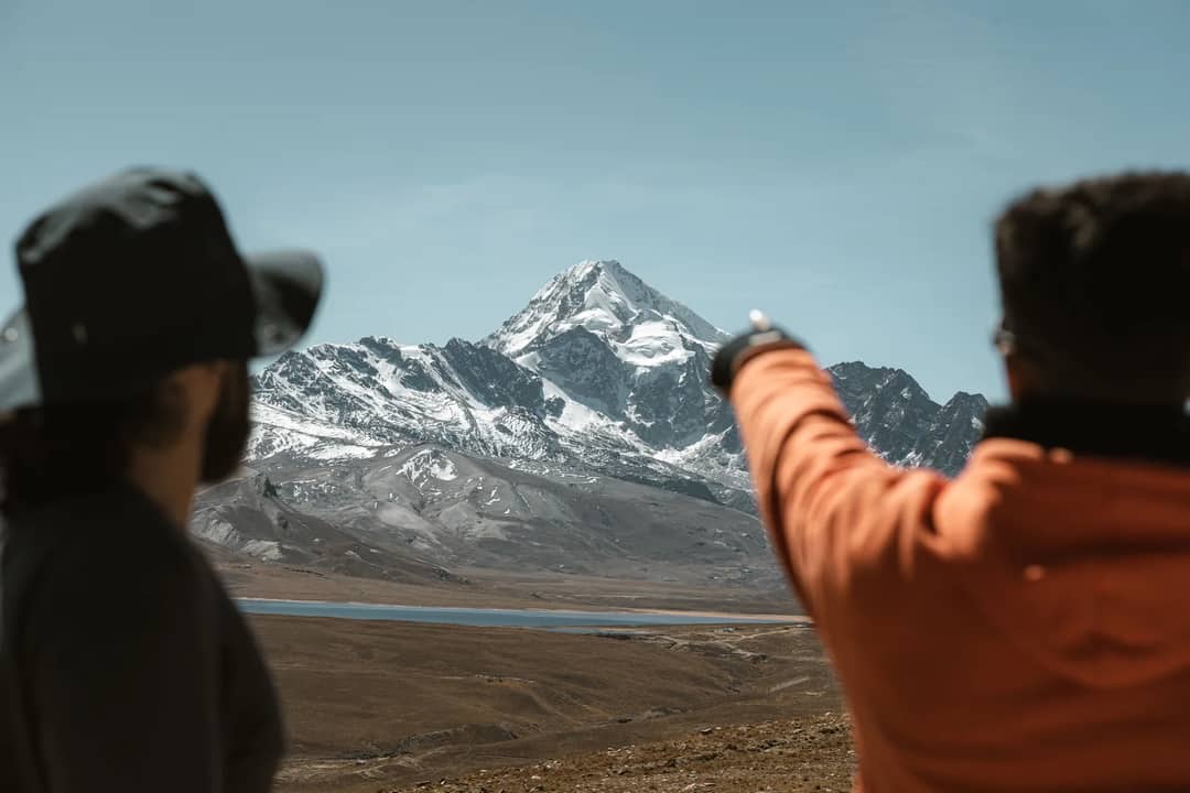 Two hikers view the stunning Huayna Potosi mountain under a clear sky.