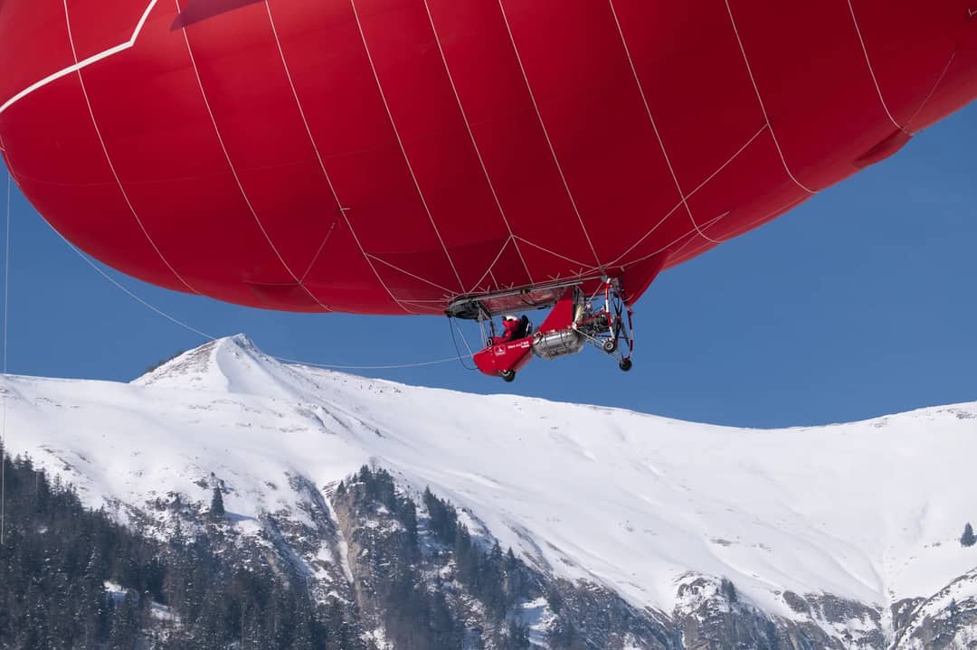 Red hot air balloon soaring over snow-covered Alps in Château-d’Œx, Switzerland.