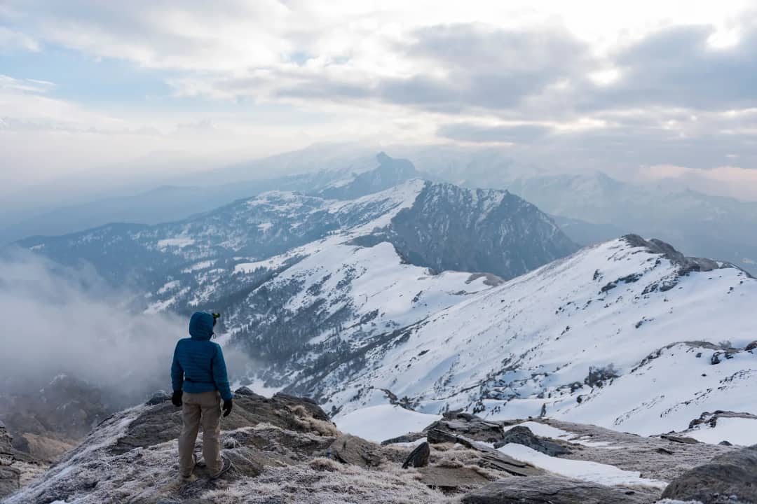 A lone traveler at a snowy mountain peak, embracing a breathtaking winter landscape.