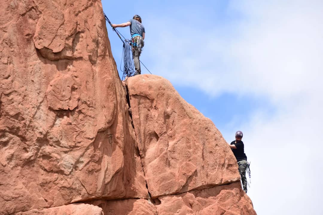 Two climbers ascending red sandstone cliffs on a clear day.