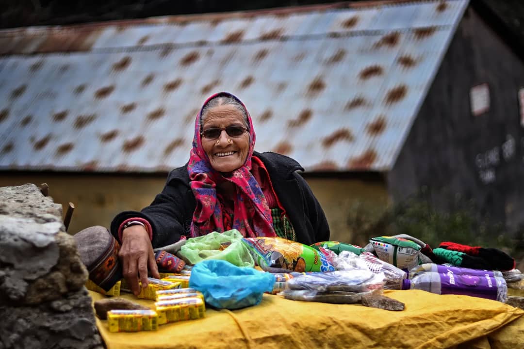 A woman selling snacks and supplies at a trailside stall in a Nepali mountain village