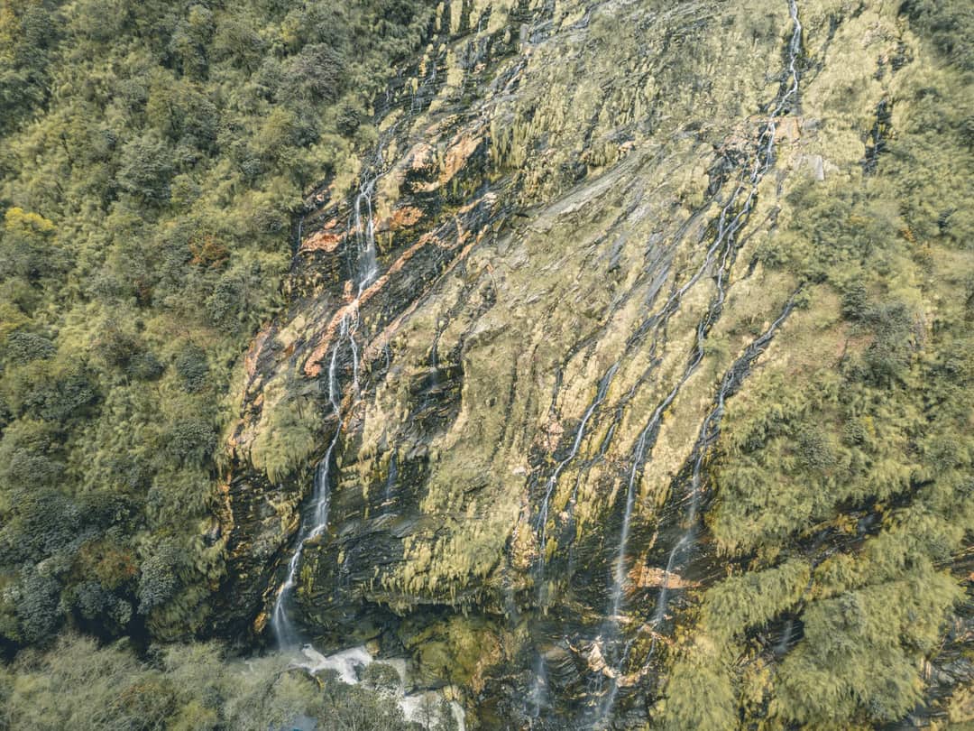 Scenic aerial capture of a beautiful waterfall cascading through lush forested mountains in Nepal's Gandaki Province.
