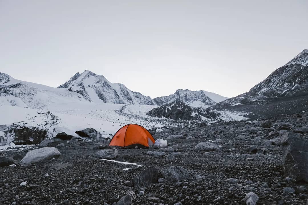 Orange tent set amidst snowy mountains in Bayan-Ölgii, Mongolia, under a clear sky.