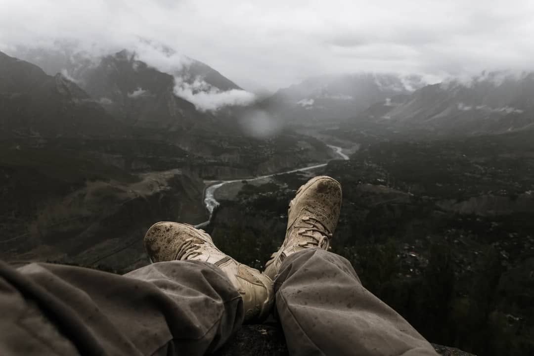 Breathtaking view of a hiker's muddy boots overlooking a misty mountain valley.