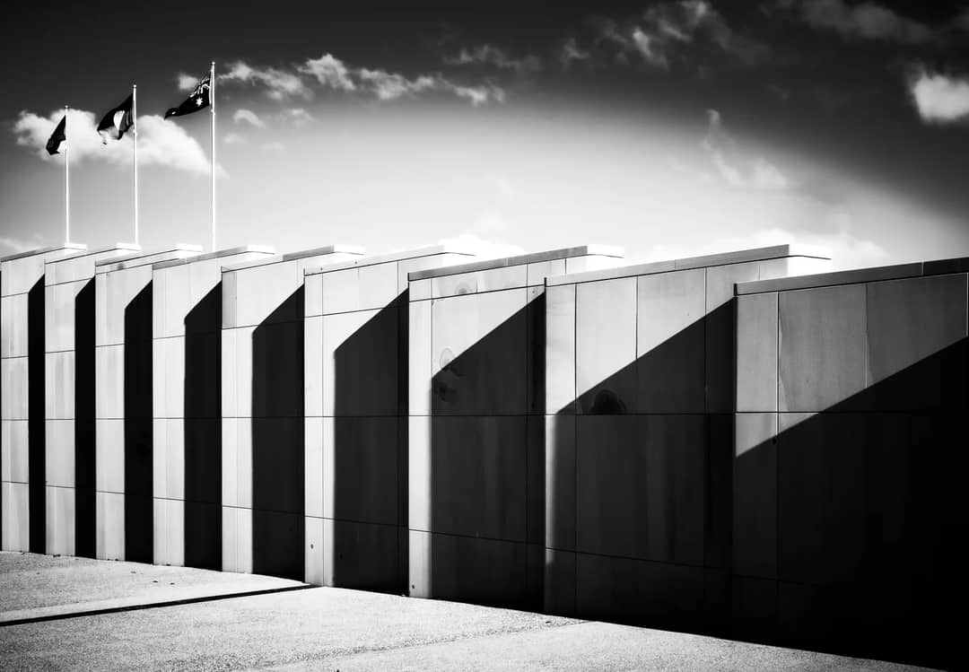 Modern building in Canberra with dramatic shadows and flagpoles under a bright sky, showcasing contemporary design.