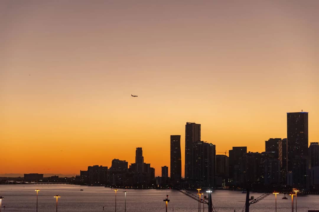 Stunning city skyline during sunset with an airplane flying above, creating a serene urban landscape.