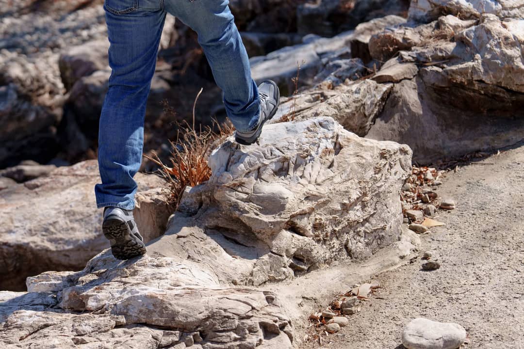 Lower view of a man in jeans hiking on a rocky path. Outdoor adventure scene.