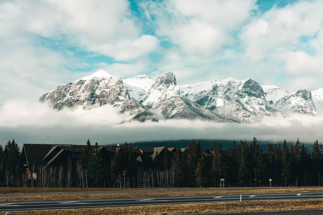 Stunning view of snow-capped mountains in Canmore, Alberta, with a forest and cabins.