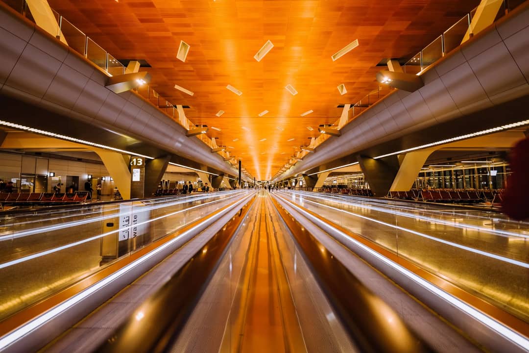 Dramatic long exposure of a modern airport terminal's moving walkalator with architectural ceiling design.