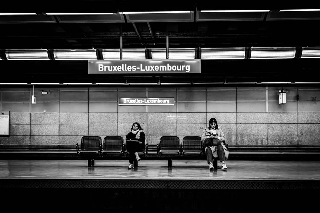 Monochrome image of two people waiting at Bruxelles-Luxembourg train station.