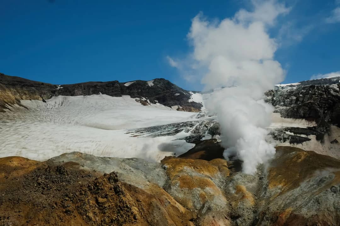 Dramatic landscape of a smoking volcano with snow-capped peaks in Kamchatka.