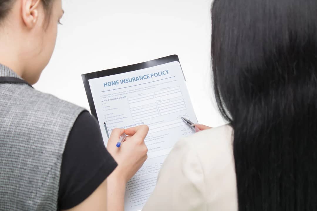 Two women examining home insurance policy form, focused on details.