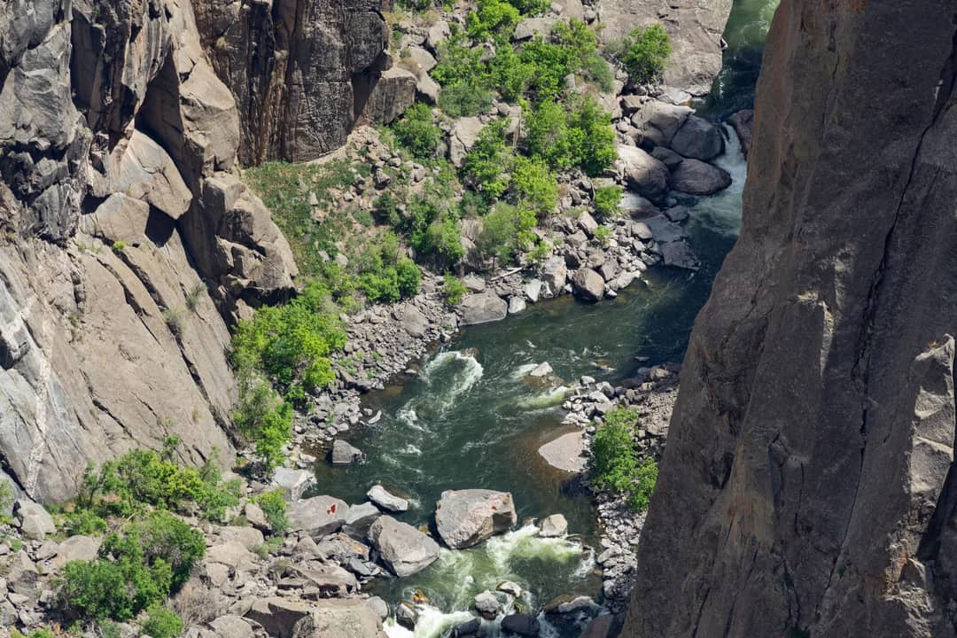Aerial view of a vibrant stream flowing through rocky canyon walls in Gunnison, showcasing summer greenery.