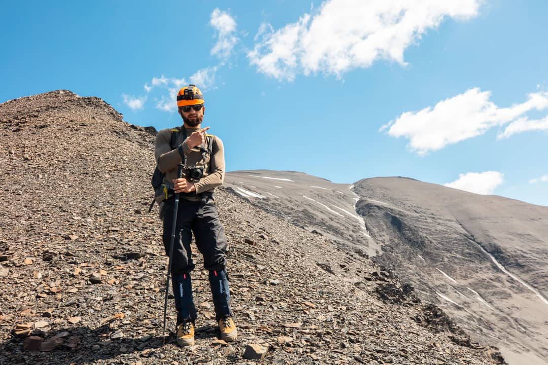 A hiker with a camera on a rocky mountain under a clear blue sky.