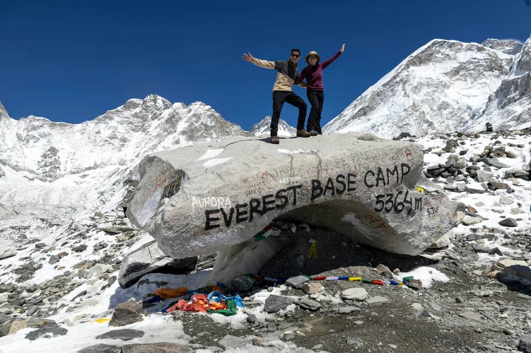 Two people celebrating at everest base camp with mountains behind
