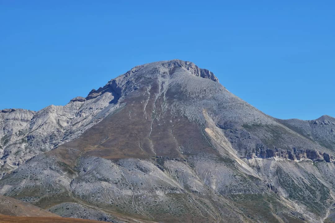 A striking view of a rocky mountain peak in a rural, arid landscape under a clear blue sky.