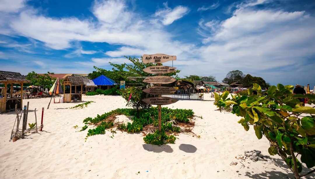 A vibrant beachscape at Koh Khai Nai featuring a prominent signpost and clear blue skies.