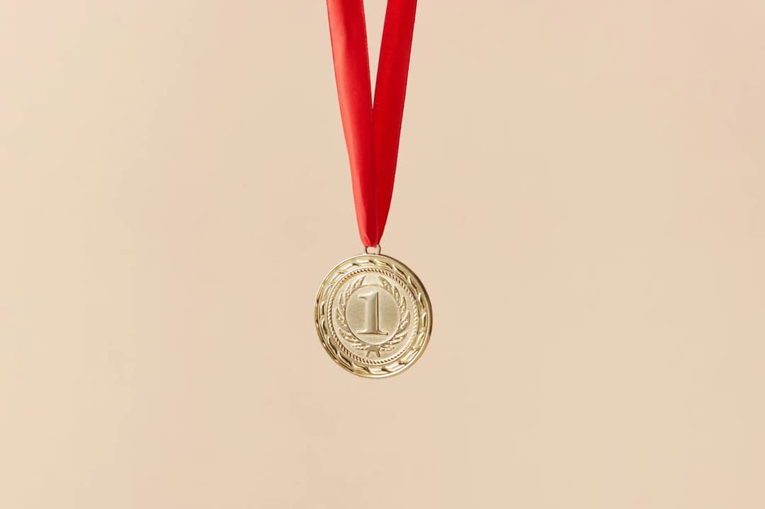 Close-up of a gold medal with a red ribbon on a beige background, symbolizing achievement.