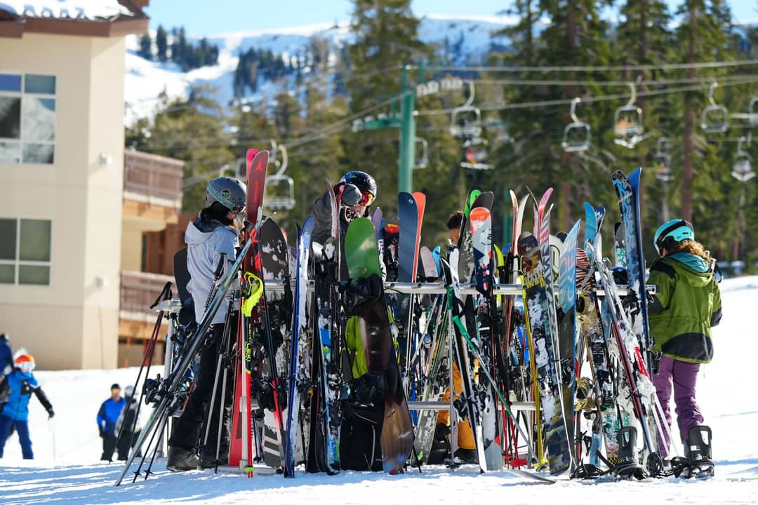 A lively scene of people gathering around ski gear at a snowy ski resort.